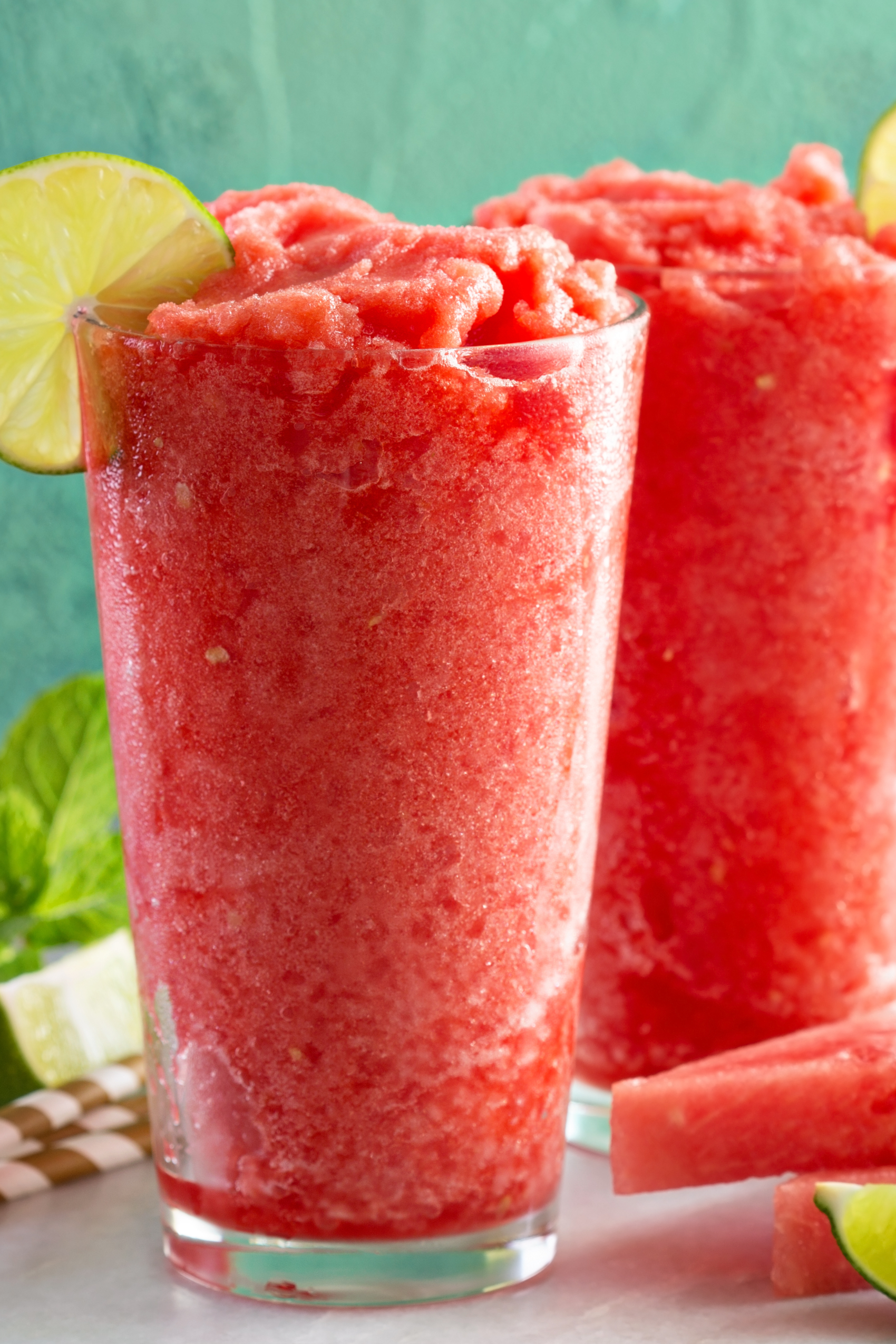 Two tall glass cups filled with watermelon wine slushies topped with a slice of lime on the rim.